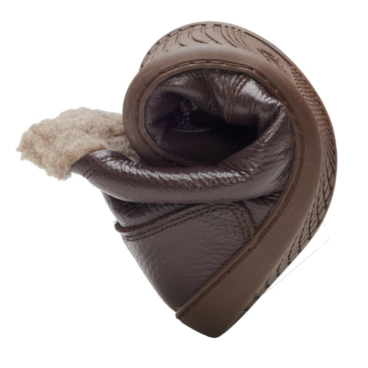 The PREQUEL Winter Nappa Brown leather shoe from ZAQQ with a cozy interior is elegantly twisted in a spiral, demonstrating its flexibility and softness against a simple white background.