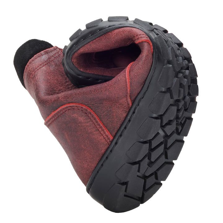 The PARQER Red from ZAQQ is a red leather boot folded in half to highlight its flexibility and over a durable black one ZAQQ Outdoor sole with deep profiles for optimal grip. The exposed stitching and worn texture give this premium nappa leather footwear a rustic, worn look.