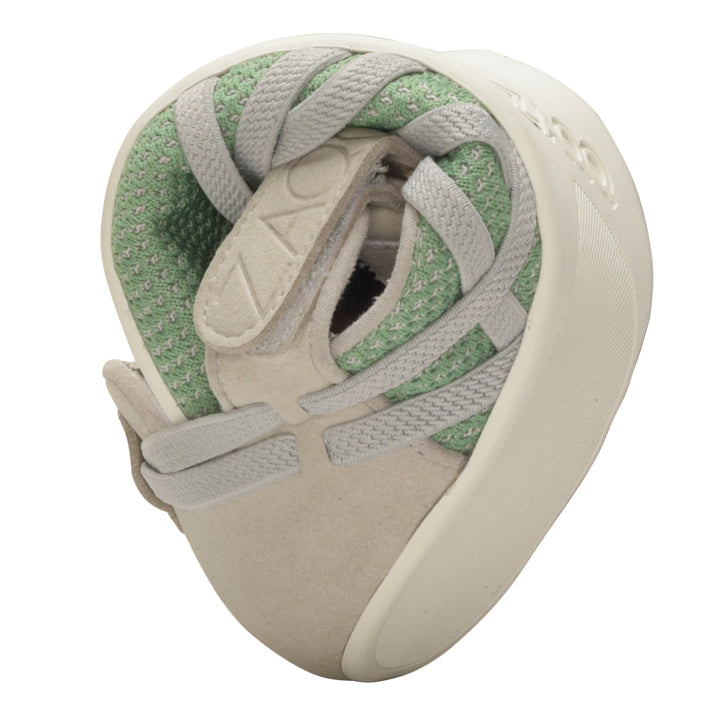 The QLAIRE Green from ZAQQ is a beige barefoot shoe with a green interior and laces that are elegantly twisted into a knot-like shape to highlight its flexibility and soft texture. The word “ZAX” is visible on the strap, while its mesh fabric design ensures breathability, all presented against a simple white background.