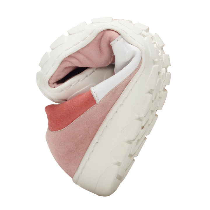 The QARTER pink sneaker from ZAQQ in pink and white is presented curved in the middle to highlight its flexibility. It features a thick, textured sole and an upper made of soft premium nappa and suede.