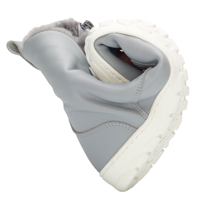 The QUINTIC Winter Blue Gray from ZAQQ is a flexible winter boot in gray with a thick white sole that is curved in the middle to highlight its flexibility. The boot is made of soft nappa leather and has a cozy, fluffy lining on the inside.