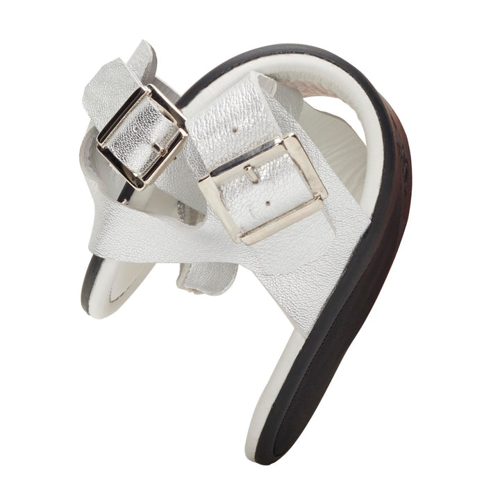 We present the QAPRI Silver from ZAQQ: an elegant silver sandal made of nappa leather with two adjustable buckle straps. The sandal features a soft white footbed and black sole for comfort and style, complemented by slip resistance for added stability. The crossed design of the buckles and straps makes them ideal for barefoot sandal lovers.