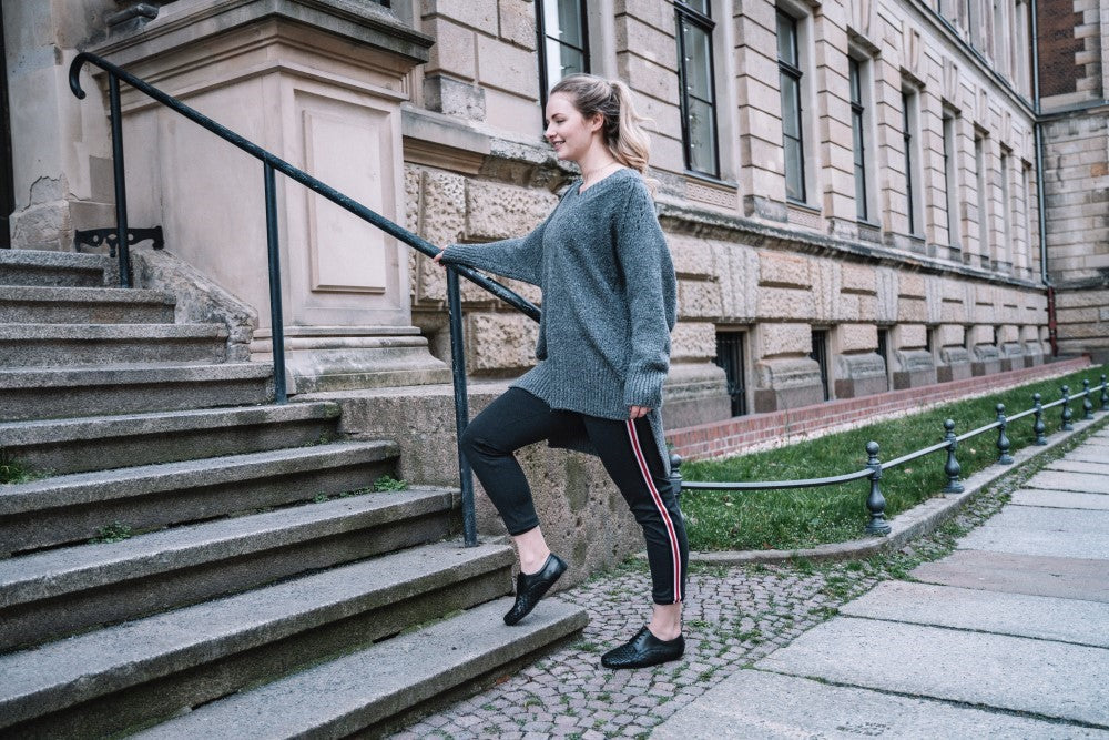 A person in a gray sweater and the IQON Plait Black by ZAQQ trains on an outside staircase next to an old building with large windows. With timeless elegance, the person smiles as they climb and enjoys the freedom of movement while holding on to the railing.