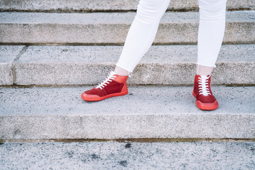 A person in white pants stands confidently on concrete steps and wears the stylish LUQQ Red high-top sneakers from ZAQQ with flexible rubber sole. The background consists of stone steps, but the focus is clearly on the stylish footwear.