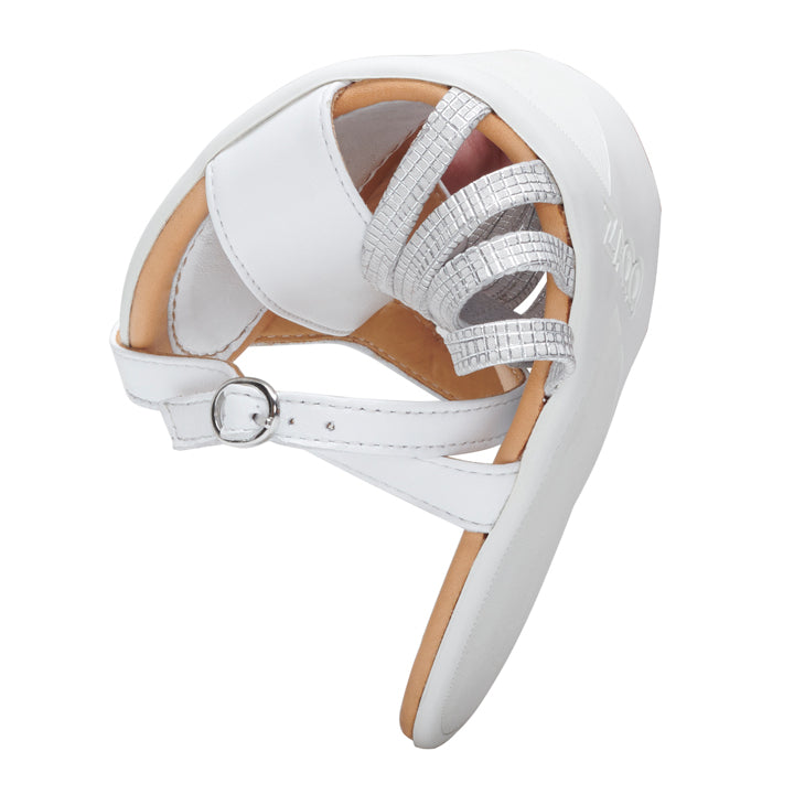 The QASSIDY Silver from ZAQQ is a white baby shoe made of smooth leather with a soft sole, side buckle and decorative silver straps across the top, perfect for those who prefer the comfort of a barefoot sandal.