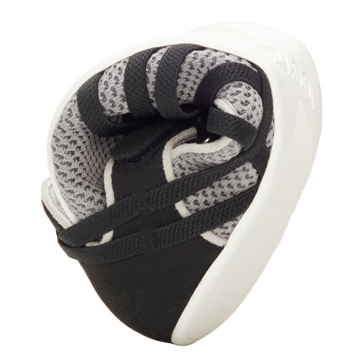 A ZAQQ QLAIRE Gray shoe with its black and gray design is shown curved in the middle to demonstrate its impressive flexibility. With a white sole and mesh upper, this product elegantly embodies the essence of ultralight ballerina shoes when viewed from the side.