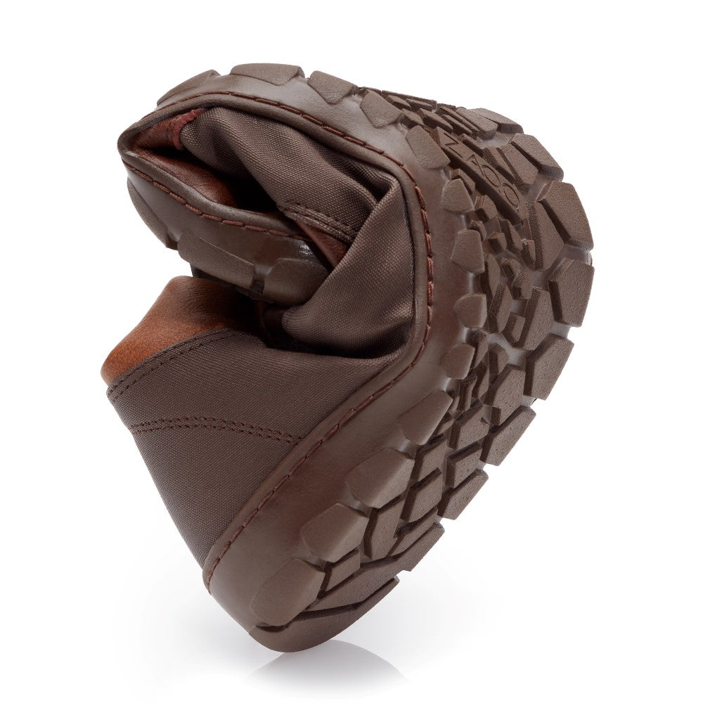 A QUEST Cuoio Waterproof barefoot shoe from ZAQQ in brown is curved in the middle to show off its flexibility with a textured sole. This shoe features a durable, waterproof design with deep treads, perfect for outdoor activities. Its visible seams and fabric emphasize its durability.