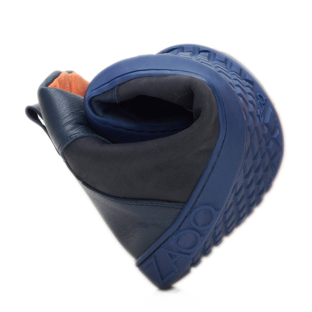 The WALQER Navy from ZAQQ is a flexible shoe in blue with a textured sole that highlights its flexibility when bending. Crafted from premium nappa leather, this barefoot boot features contrasting black and orange elements that enhance its unique and stylish design.
