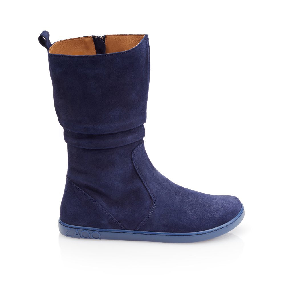 The ZAQQ QOM Blue Single Boot features navy blue goat suede and a flat blue sole with the signature ZAQQ Barefoot sole design. It features a mid-calf height, a relaxed fit, a side zip and loop for comfortable wear, along with an embossed brand logo near the heel and a tan lined interior.