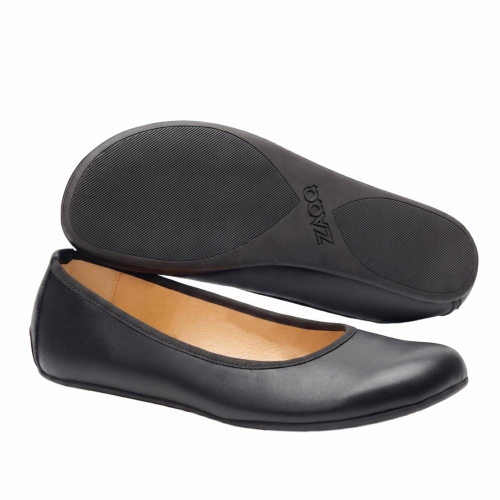 Ausgestellt wird ein Paar schwarze Ballerinas ZAQQ QARMA. Ein Schuh liegt auf der Seite und zeigt die glatte schwarze Sohle und das Fußbett, während der andere aufrecht steht und eine glatte Lederoberfläche offenbart, die an die Anmut einer Ballerina erinnert, ergänzt durch ein warmes braunes Innenfutter.