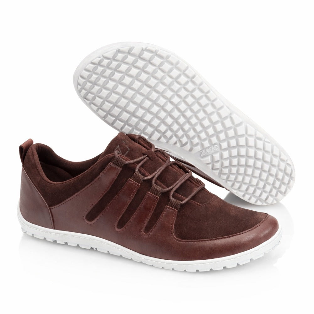 Die ZAQQ SHOQQ Dark Brown Sneaker kombinieren Leder und Wildleder für einen schicken Look, der durch weiße Gummisohlen abgerundet wird. Diese Barfußschuhe haben dekorative Schnürsenkel und ein einfaches Slip-On-Design, wobei ein Schuh das Gittermuster auf seiner Sohle hervorhebt.