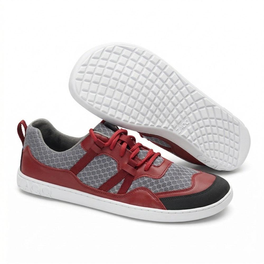 Ein Paar SQATE Red-Sportschuhe von ZAQQ mit Obermaterial aus rotem und grauem Mesh, schwarzen Akzenten und roten Schnürsenkeln. Sie sind für ultimativen Tragekomfort konzipiert und haben eine cremefarbene Sohle mit strukturiertem Gittermuster und das Markenlogo OO auf der Außensohle.