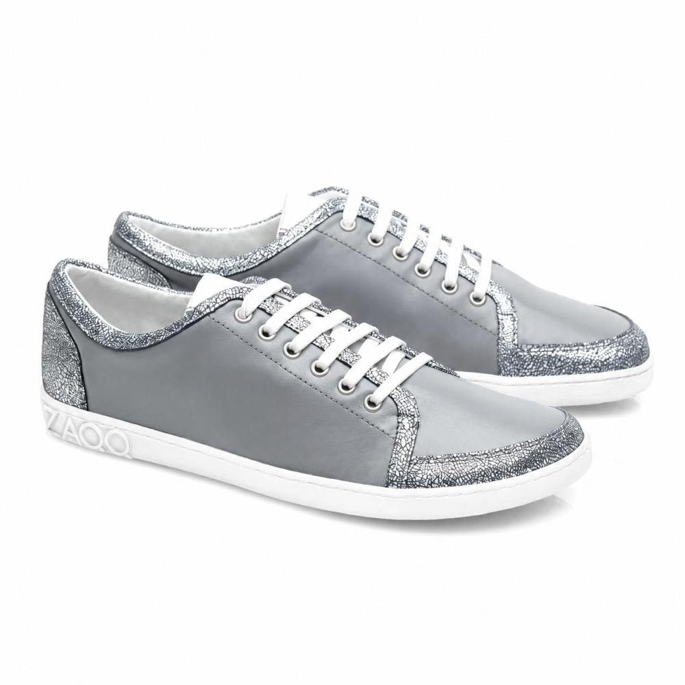 The TIQQ Grey Silver Sneakers by ZAQQ captivate with their simple design made from soft nappa leather with white laces and silver glitter accents, complemented by white soles and a subtle logo on the heel, offering the perfect blend of style and comfort for any occasion.