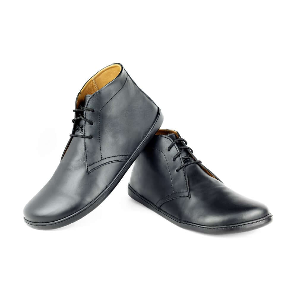 Ein Paar elegante schwarze Lederschuhe ist auf einem weißen Hintergrund abgebildet. Ein Schuh steht aufrecht, während der andere daran lehnt. Sie haben eine glatte Oberfläche, dünne schwarze Schnürsenkel und abgerundete Zehenpartie, mit einem leicht glänzenden Schimmer und hellbraunem Innenfutter.